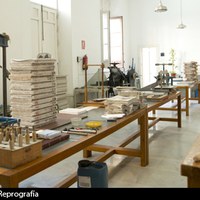 Vista general del Taller de Encuadernación. Taller de grandes dimensiones  en que la maquinaria, de tracción manual, está distribuida  de manera ordenada: prensas, cizallas, guillotina, telares, etc. A destacar el telar de madera para coser los libros a mano. El taller ha mantenido el oficio en su forma tradicional hasta el día de hoy. ©ICAS-SAHP, Dpto. Reprografía