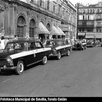 En la acera más cercana a la Casa Consistorial vemos la parada del servicio público de  taxis con los característicos SEAT 1500 de color amarillo y negro. En esas mismas fechas se instauró un estricto control sobre la uniformidad de la indumentaria de los conductores. 1967-1968.  ©ICAS-SAHP, Fototeca Municipal de Sevilla, fondo Gelán